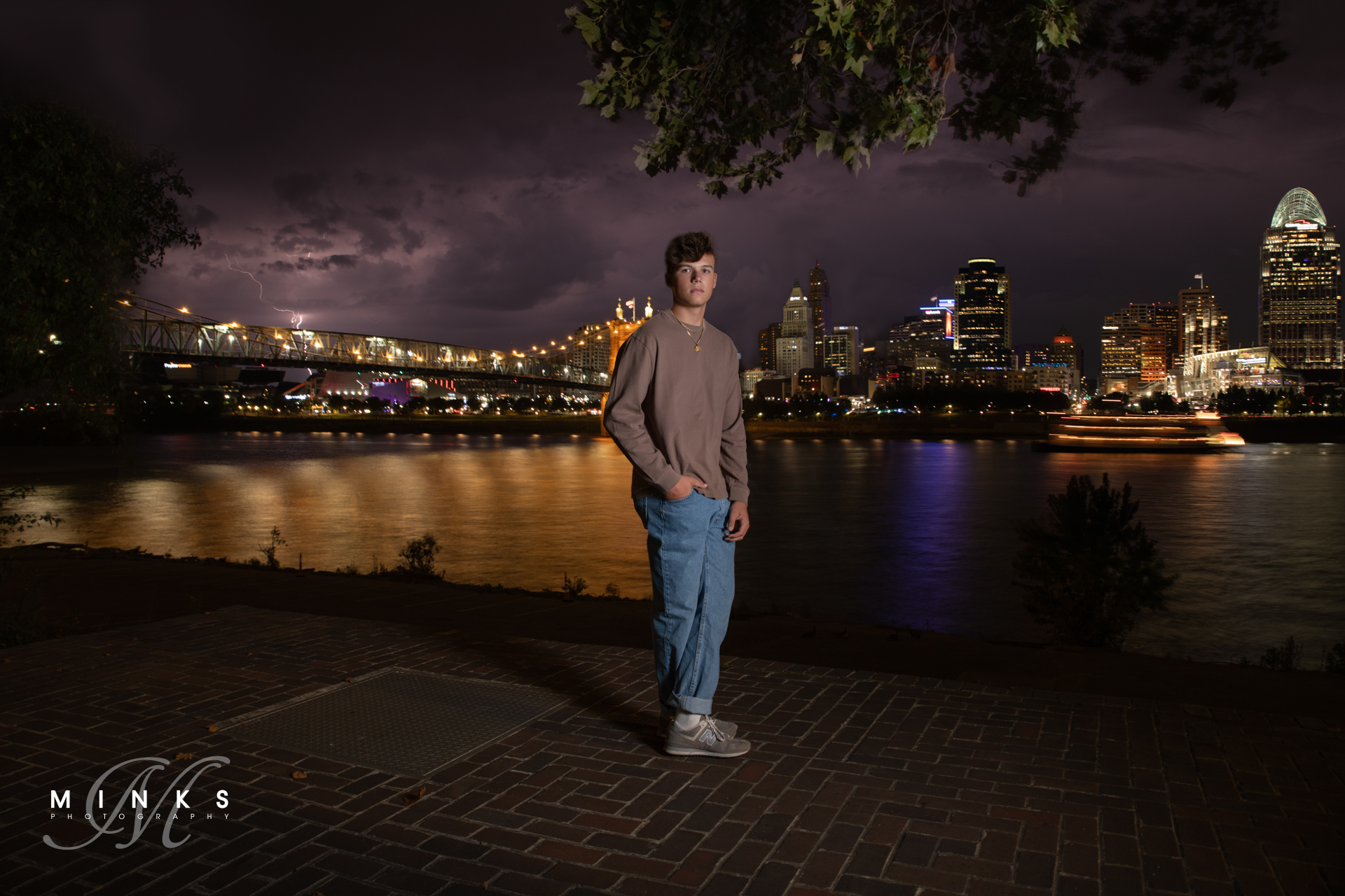 senior guy in front of Cincinnati skyline at night with lightning