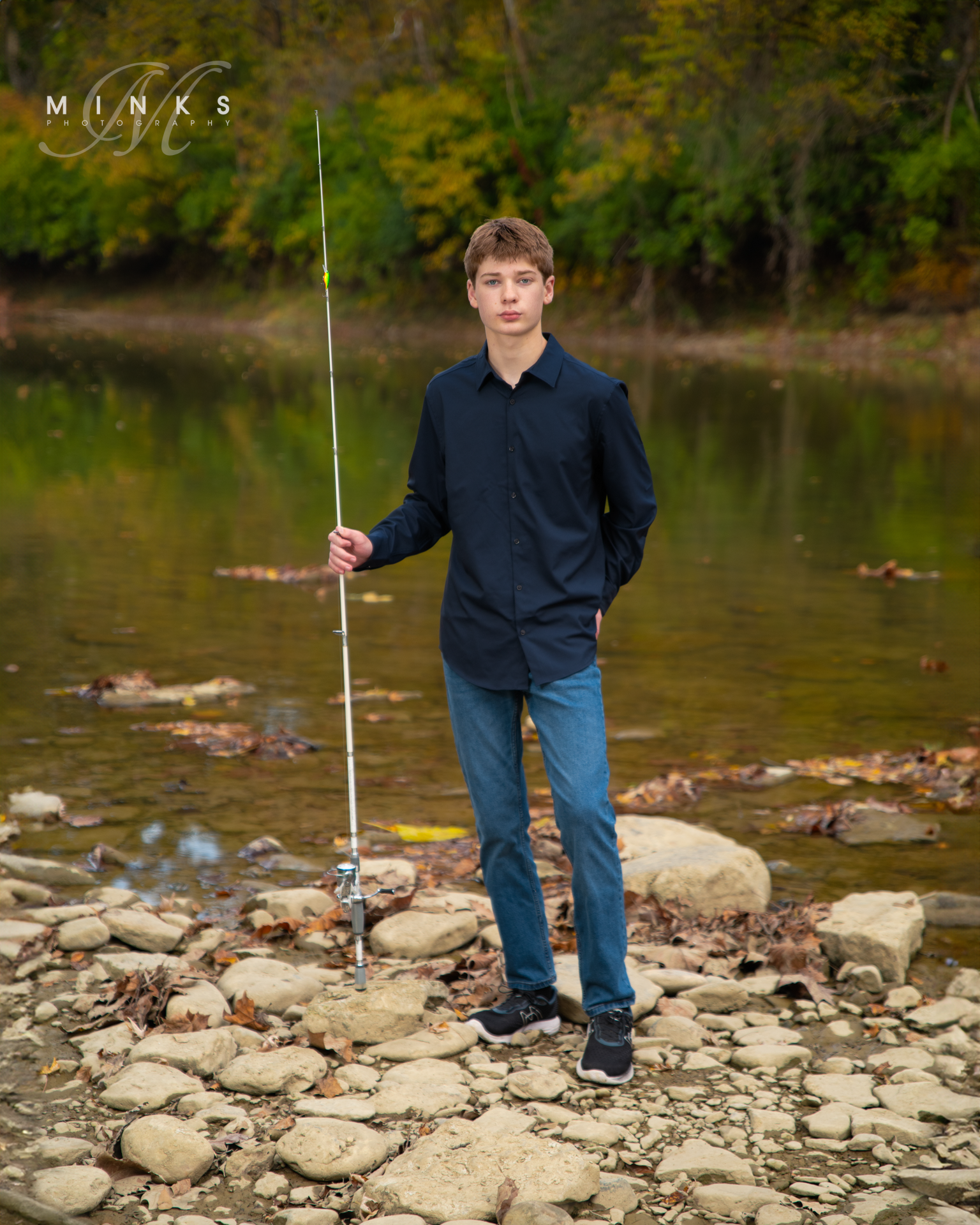 senior guy standing beside a river with fishing pole
