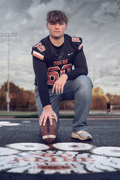 senior guy kneeling with football in front of tiger paw