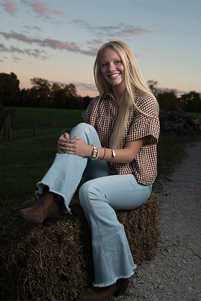 senior girl sitting on bale of hay at farm