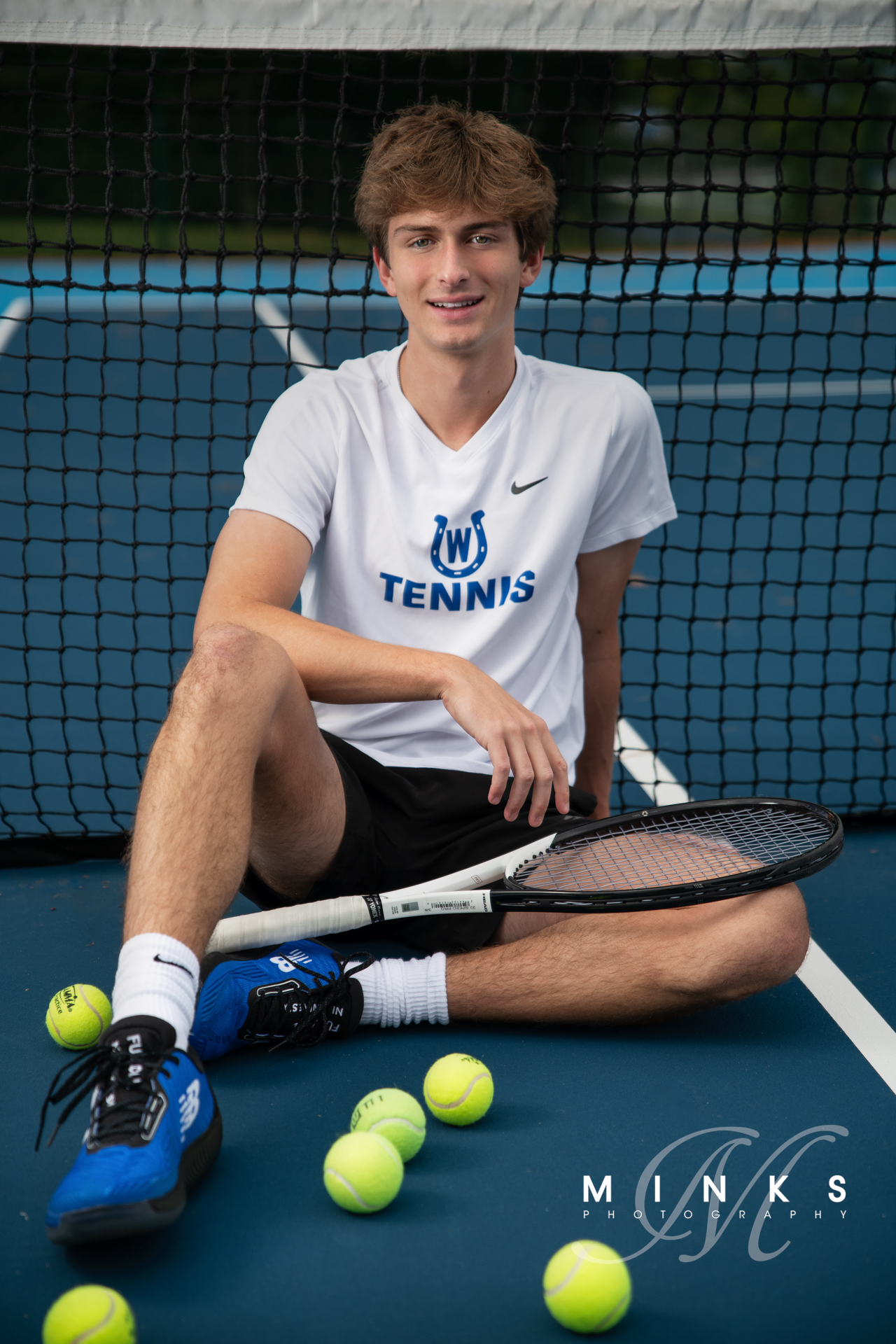 high school senior guy sitting on tennis court with tennis racquet and tennis balls