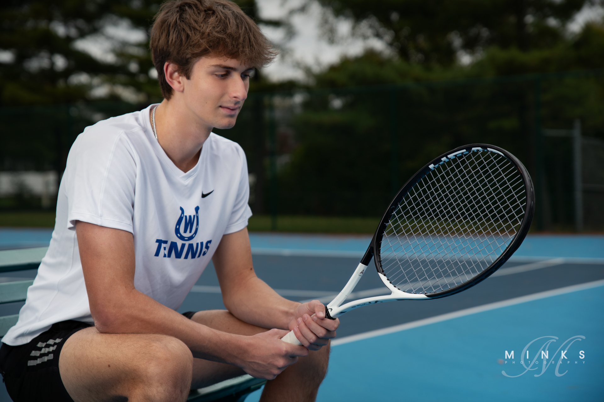high school senior guy tennis plying sitting on a bench looking at his racket