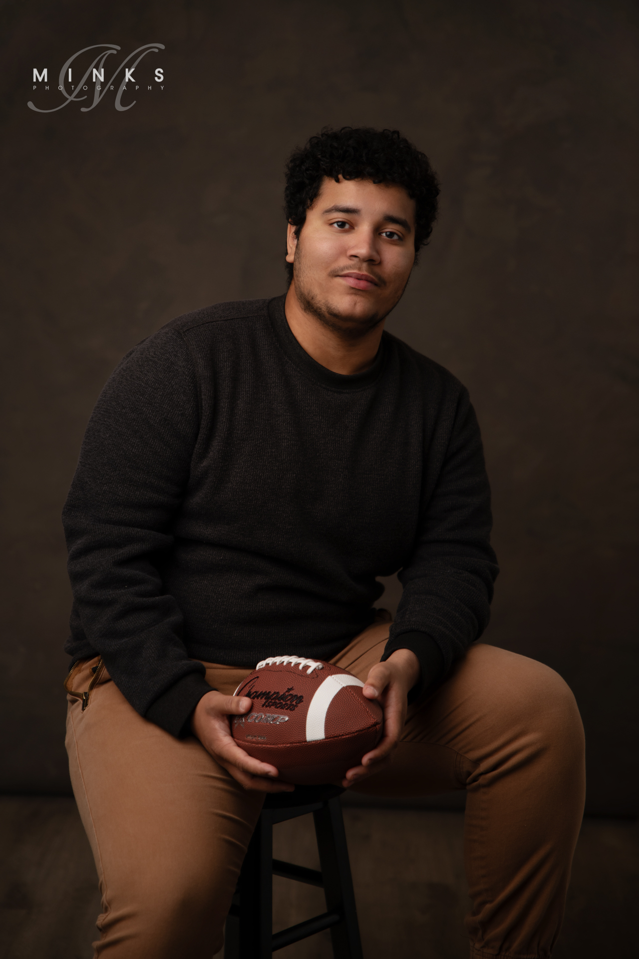 High School senior football player sitting on a stool holding a football