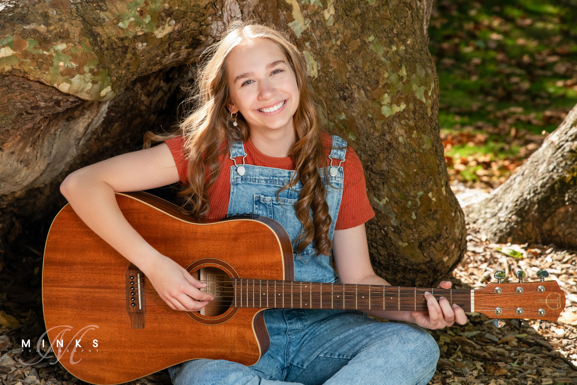high school senior girl sitting in front of a tree playing a guitar