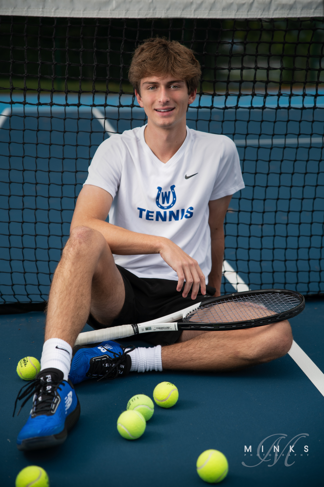 high school senior guy sitting on tennis court with tennis racquet and tennis balls